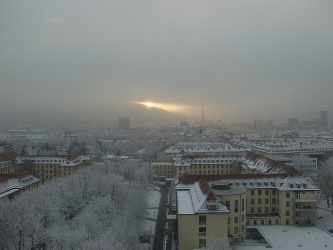 Sonneaufgang im Nebel hinter den schneebedeckten Dächern Freiburgs